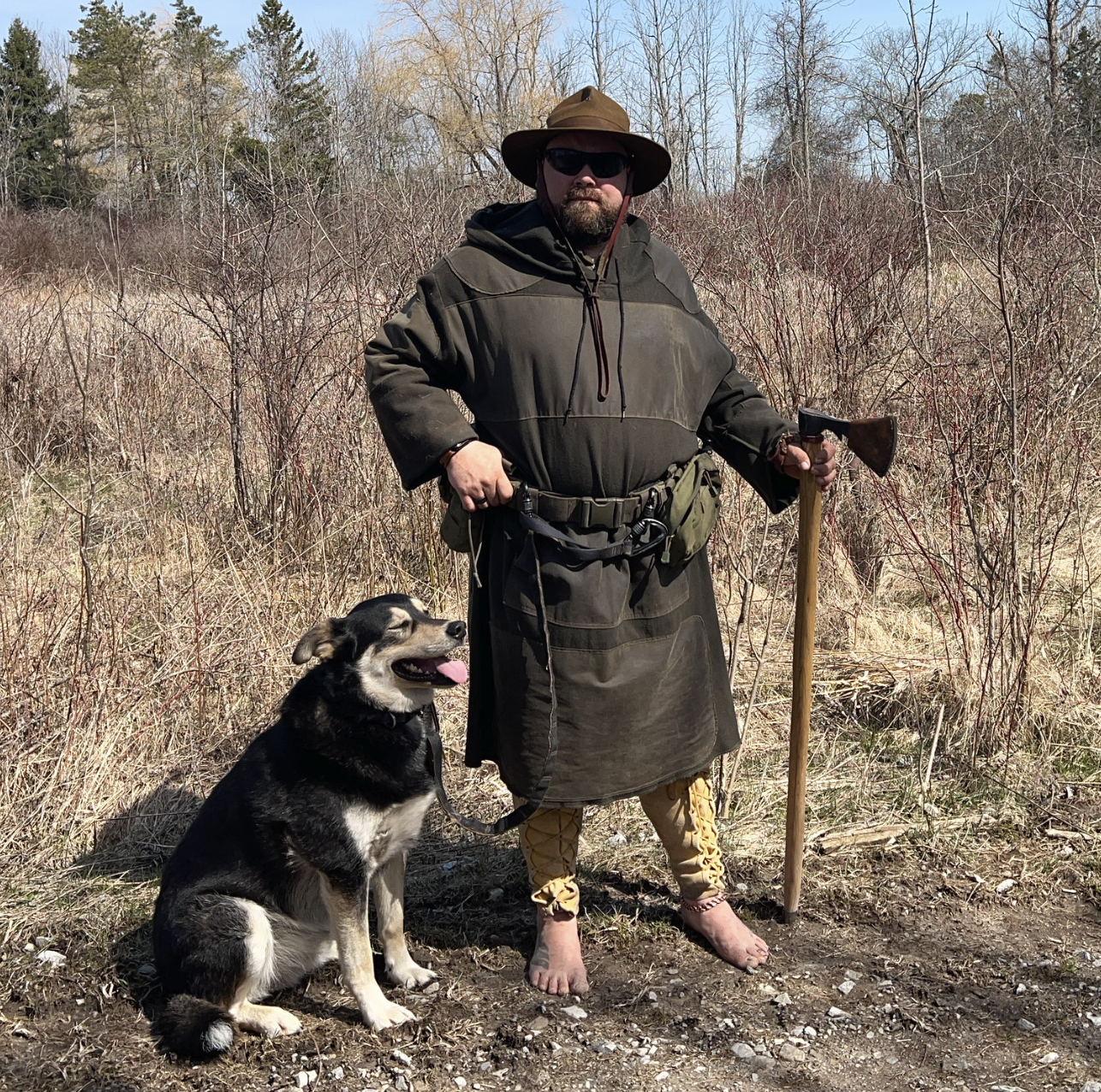 Man with a dog in old fashioned clothing standing barefoot in the forest