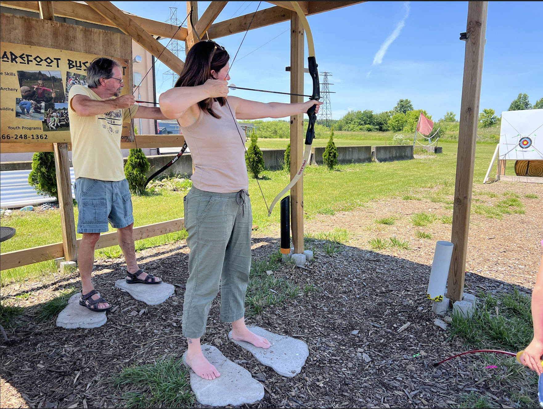 Woman standing barefoot holding a bow and arrow doing archery